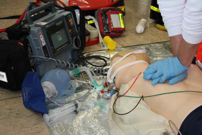 Bild zeigt Mitarbeiter bei der Herz-Lungen-Wiederbelebung an einer Übungspuppe. Angeschlossen sind ein Defibrillator und ein Beatmungsbeutel.