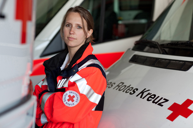 Mitarbeiterin des Rettungsdienstes lehnt sich an einen Rettungswagen.