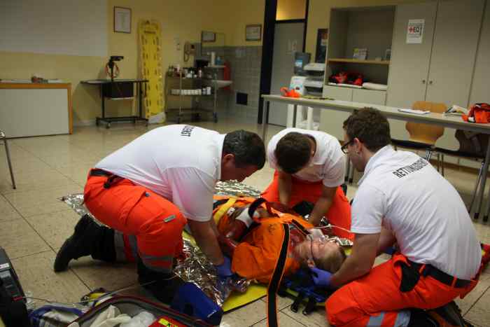 3 Sanitäter des Roten Kreuzes haben im Schulungsraum einen Notfalldarsteller mit einem Spine Board fixiert.